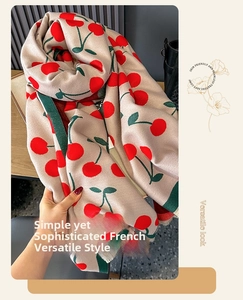 Detail of beige cashmere-feel scarf featuring red cherry patterns and soft fringe edges