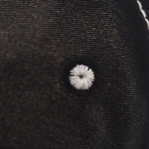 Macro detail of white star embroidery on black washed denim fabric with stitched edge