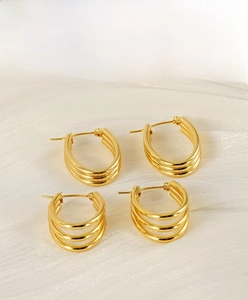 Detailed view of gold U-shaped multi-layered earrings on white silk fabric background