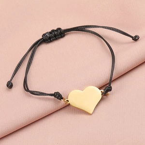 Macro detail of polished gold heart charm on a black woven adjustable cord bracelet