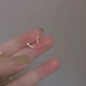 Detailed close-up of golden curved zircon stud earrings held between fingertips