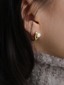 Elegant gold S925 earrings with white natural pearls worn by a model on dark hair background