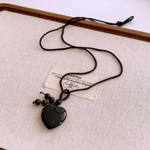 Close-up of polished black heart pendant on a woven rope cord over a linen texture