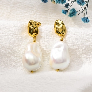 Detailed shot of gold drop earrings with baroque pearls on a textured white fabric