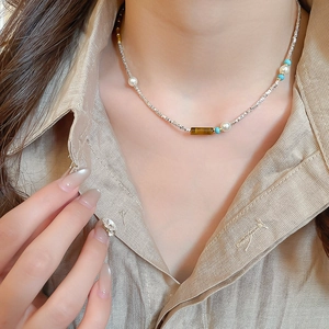 Detail of beaded necklace featuring tiger eye stone, pearls, and silver beads on model