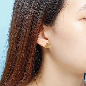 Close-up of golden hollow heart earrings with twisted texture worn by a model