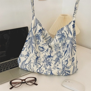 Blue floral canvas tote bag on a desk with a laptop and lamp in a lifestyle setting