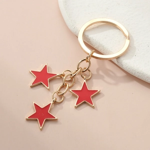 Detailed view of gold chain keychain with three red enamel star charms on pink background