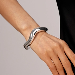 Dettaglio di un bracciale a fascia argento minimalista con finitura lucida e ondulata