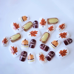 Thanksgiving press-on nails with maple leaf and pumpkin designs on white background