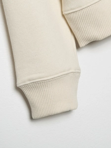 Detailed close-up of ribbed cuffs on a cream-colored cotton knit sweatshirt for women