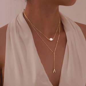 Detail of a gold double-layer Y-necklace featuring a white pearl and letter A pendant