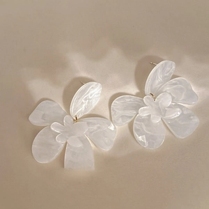 Detailed view of white resin flower earrings with marble texture on beige fabric