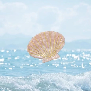Pink shell hair claw with marble texture and gold accents on a beach background