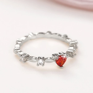 Macro close-up of a silver ring featuring a red heart zircon and white round crystals