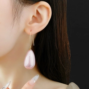 Dettaglio di orecchino con perla rosa a goccia e gancio dorato indossato da una modella