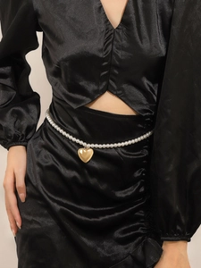 Detail showing white pearl waist chain with a polished gold heart pendant on black satin