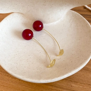 Detail of red cherry drop earrings with gold hooks on a white decorative shell plate