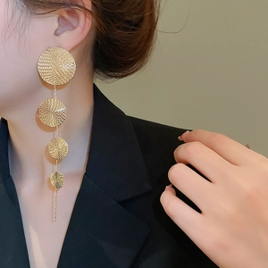 Detail of long gold drop earrings with textured round discs worn by a female model