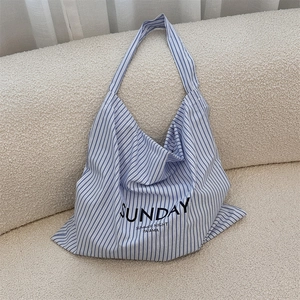 Close-up of blue and white striped canvas tote bag with SUNDAY lettering on a sofa