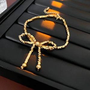 Close-up of golden bow bracelet featuring square metal beads on black display tray