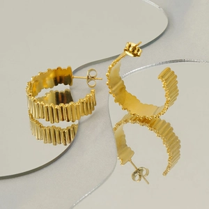 Detailed view of gold-colored ribbed hoop earrings reflecting on a mirror surface