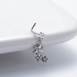 Macro shot of silver L-shaped nose stud with zircon floral pendant on white surface