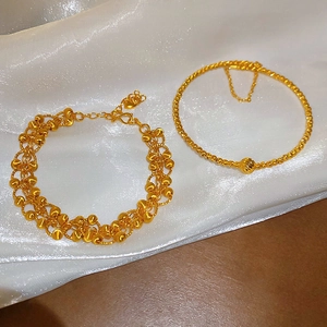 Detailed view of 24K gold plated bead bracelets on a white silk and wood surface
