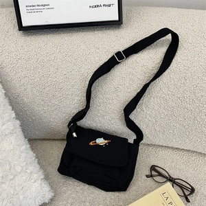 Detail of black canvas crossbody bag with colorful planet embroidery on beige sofa