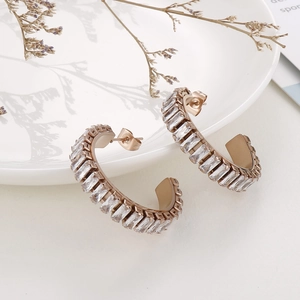 Detail of rose gold C-shaped hoop earrings with baguette-cut white zircon on a white plate