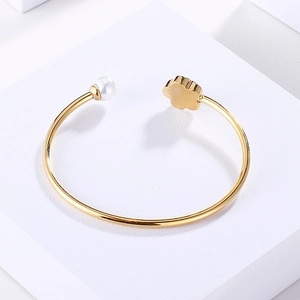 Close-up of a gold open cuff bracelet featuring a white pearl and a five-petal flower detail