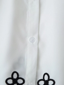 Detailed close-up of white shirt featuring black floral embroidery and neat button placket
