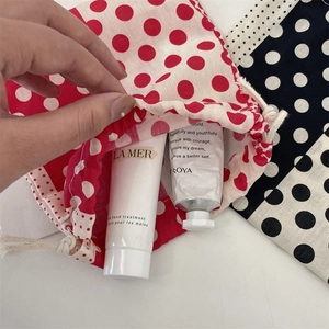Detail view of red polka dot drawstring cotton pouch holding hand cream tubes