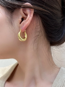 Close-up of model wearing polished gold chunky teardrop earrings with mirror finish