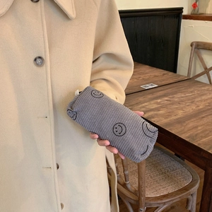 Detail of grey corduroy cosmetic bag with black smiley embroidery held by a model