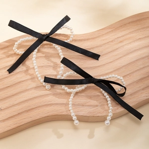 Detail of silk bow earrings with white pearls on a textured wooden display tray