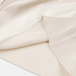 Detail shot of beige satin dress hemline showing precision stitching and fabric texture