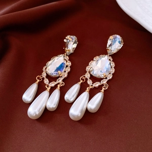 Macro detail of 18k gold plated pearl drop earrings on luxurious red silk fabric