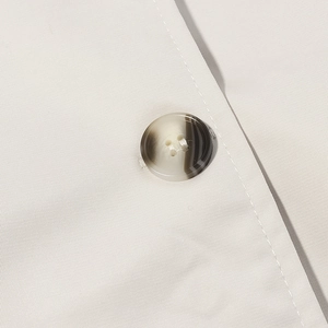 Detailed macro shot of a four-hole resin button on off-white twill trench coat fabric