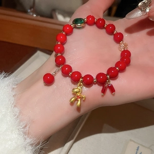 Detail of red beaded bracelet featuring a gold horse charm and green gemstone accent