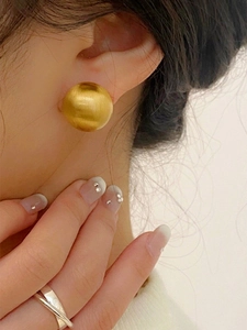 Detail of a brushed gold spherical stud earring worn by a model with elegant styling