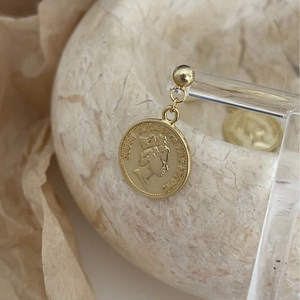 Macro shot of gold Elizabeth II coin earrings hanging on a display with vintage props