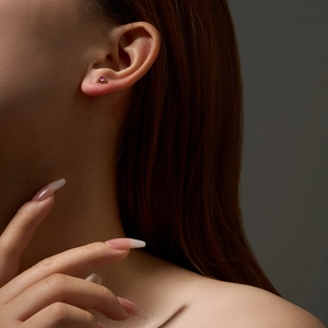 Detailed close-up of a golden triangle stud earring featuring a purple gemstone on a model