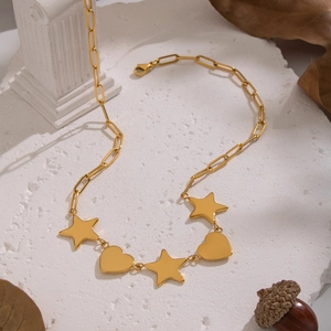 Vue détaillée du collier doré avec pendentifs étoile et cœur sur surface en pierre blanche