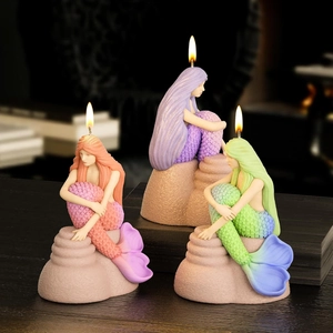 Three detailed 3D mermaid scented candles on stone bases on a rustic wooden table