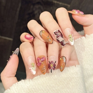 Almond shaped press-on nails with orange floral art and golden 3D metallic charms