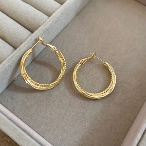 Detail view of gold intertwined hoop earrings with twisted and smooth texture in a jewelry box