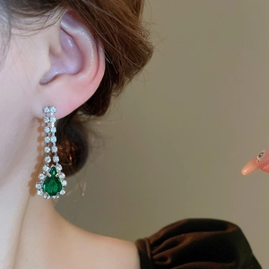 Detailed view of silver dangle earrings featuring emerald teardrop stones and tassels