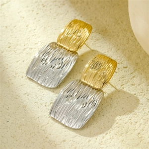 Détail de boucles d'oreilles géométriques bicolores avec texture martelée et effet de vagues