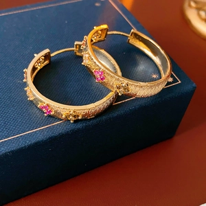 Détail de boucles d'oreilles créoles fleurs en plaqué or 18K avec pierres rouges et jaunes